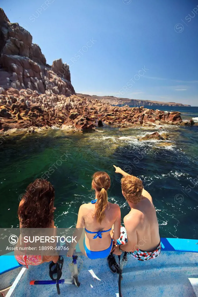 three tourists sitting on the edge of a boat with snorkeling gear at los islotes national marine park espiritu santo island, la paz baja california me...