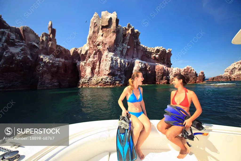 two tourists sitting on the edge of a boat with snorkeling gear at los islotes national marine park espiritu santo island, la paz baja california mexi...