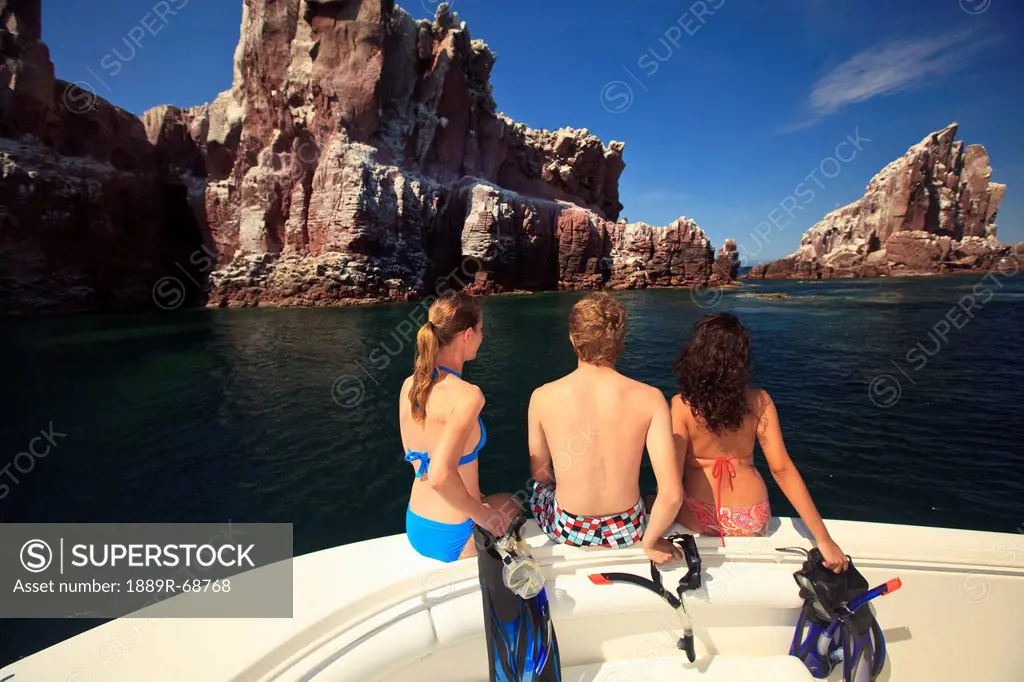 three tourists with snorkeling gear sitting on the edge of a boat at los islotes national marine park espiritu santo island, la paz baja california me...