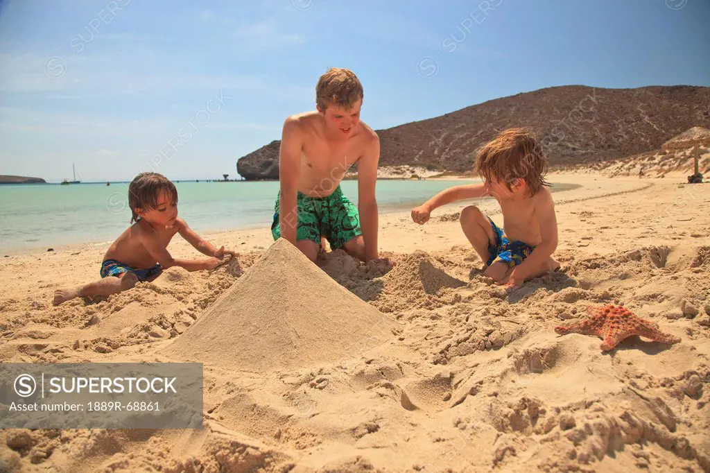 three boys play in the sand at the water´s edge at los islotes national marine park espiritu santo island, la paz baja california mexico