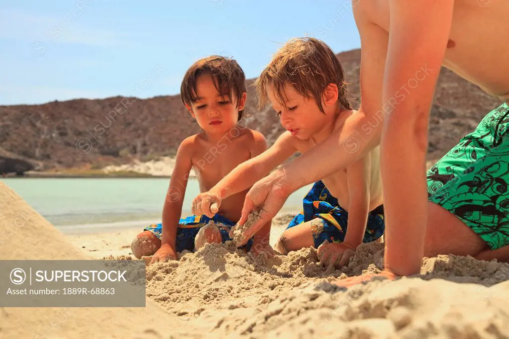 three boys play in the sand at the water´s edge at los islotes national marine park espiritu santo island, la paz baja california mexico