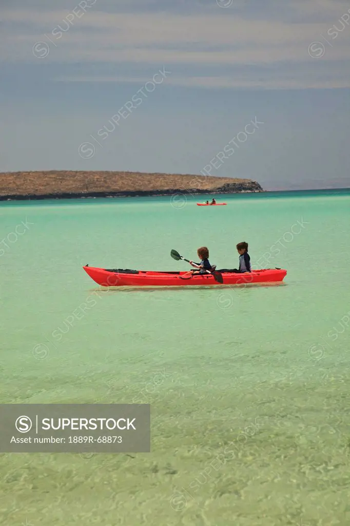 two young boys paddling in a red boat at los islotes national marine park espiritu santo island, la paz baja california mexico