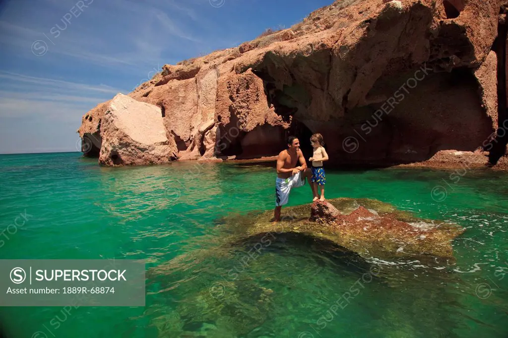 a father and son standing on a rock in the ocean at los islotes national marine park espiritu santo island, la paz baja california mexico