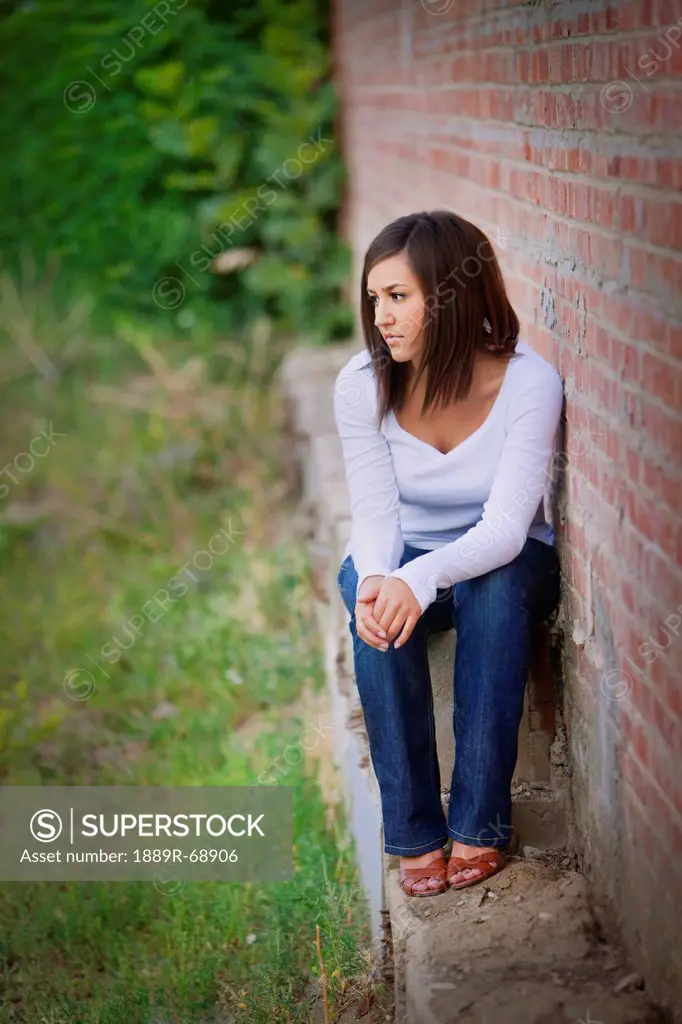 a young woman sits along along a brick wall, edmonton alberta canada