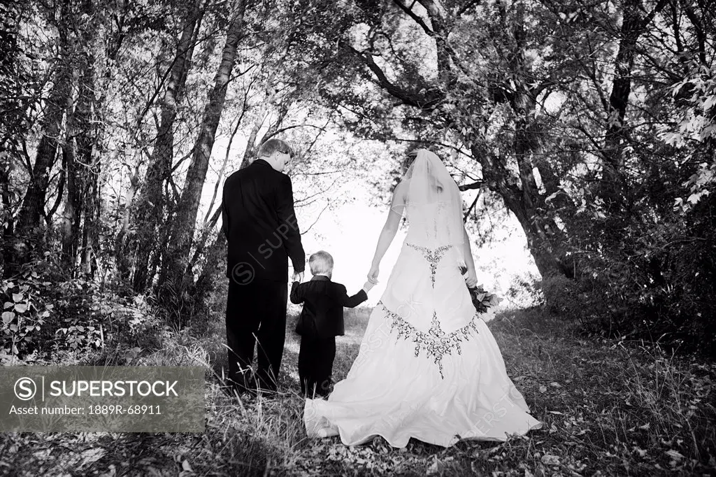 a bride and groom walking and holding a young boy´s hand in between them, edmonton alberta canada