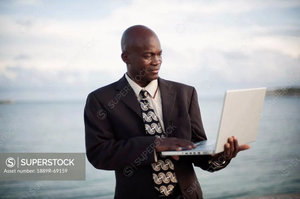 a businessman using a laptop computer by the water´s edge, south caicos turks and caicos islands