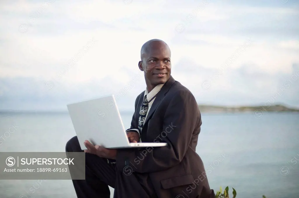 a businessman working on a laptop computer by the water´s edge, south caicos turks and caicos islands