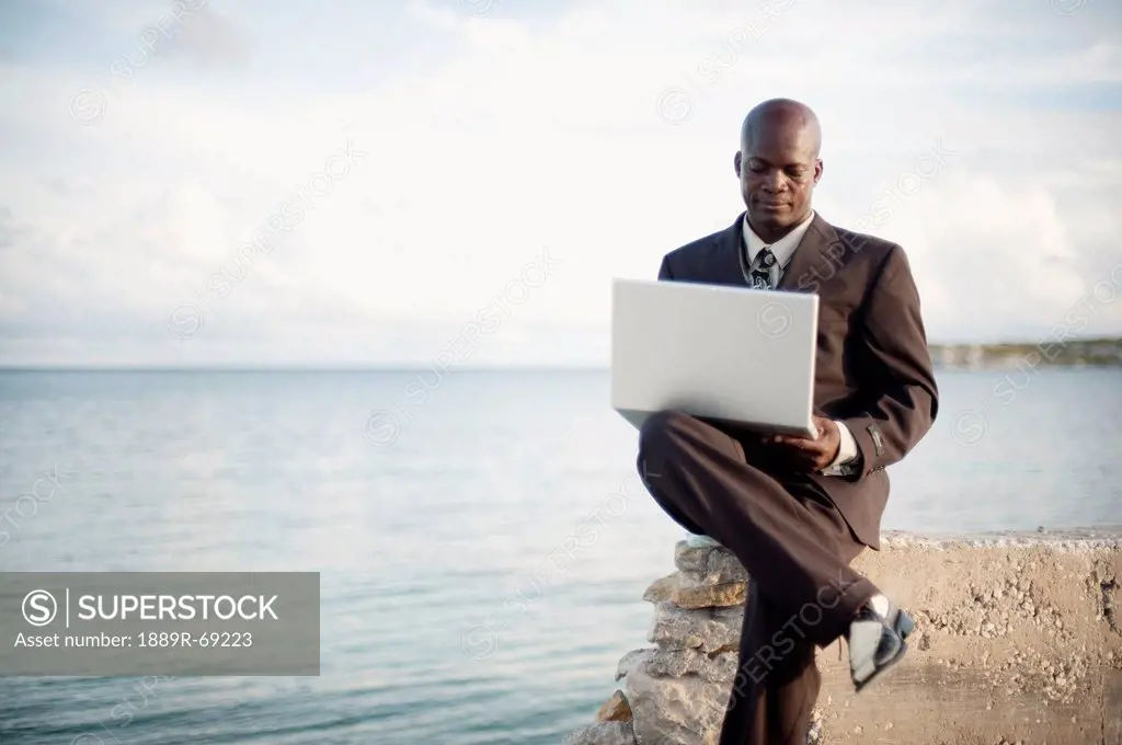 a businessman using a laptop computer on the water´s edge, south caicos turks and caicos islands