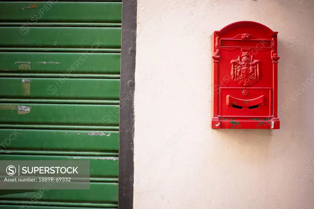 a red mailbox mounted on a white wall beside a green door, genoa liguria italy