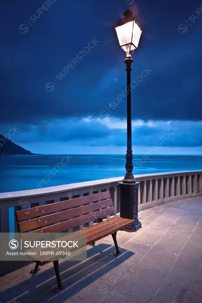 a bench and light post along the railing on the coast, camogli liguria italy