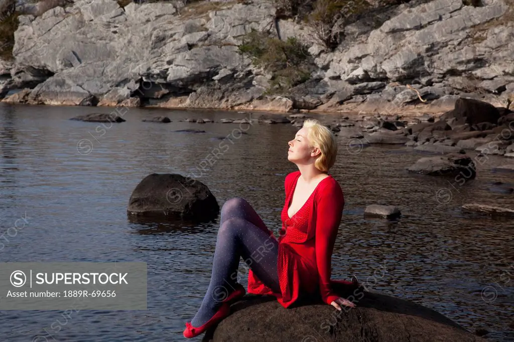 a young woman basks in the sunshine while sitting on a large rock on muckross lake, killarney county kerry ireland