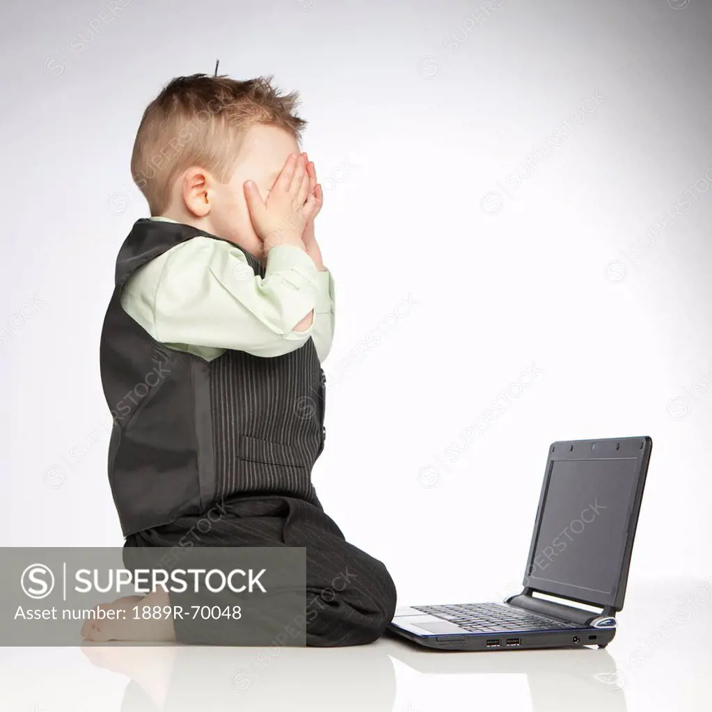 a young boy covers his eyes as he sits in front of a laptop computer, edmonton alberta canada