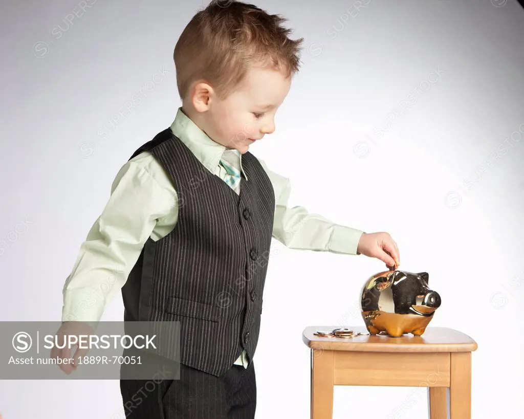 a young boy wearing a vest puts money into a piggy bank, edmonton alberta canada