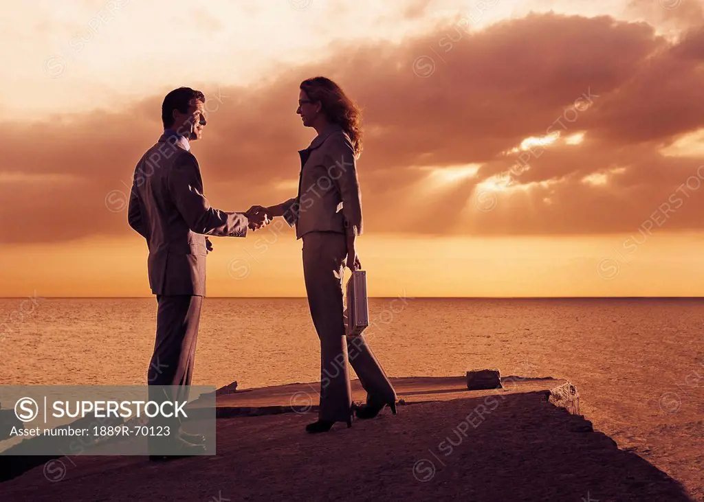 a businessman and businesswoman shaking in agreement on a dock along the water at sunset, tarifa cadiz andalusia spain