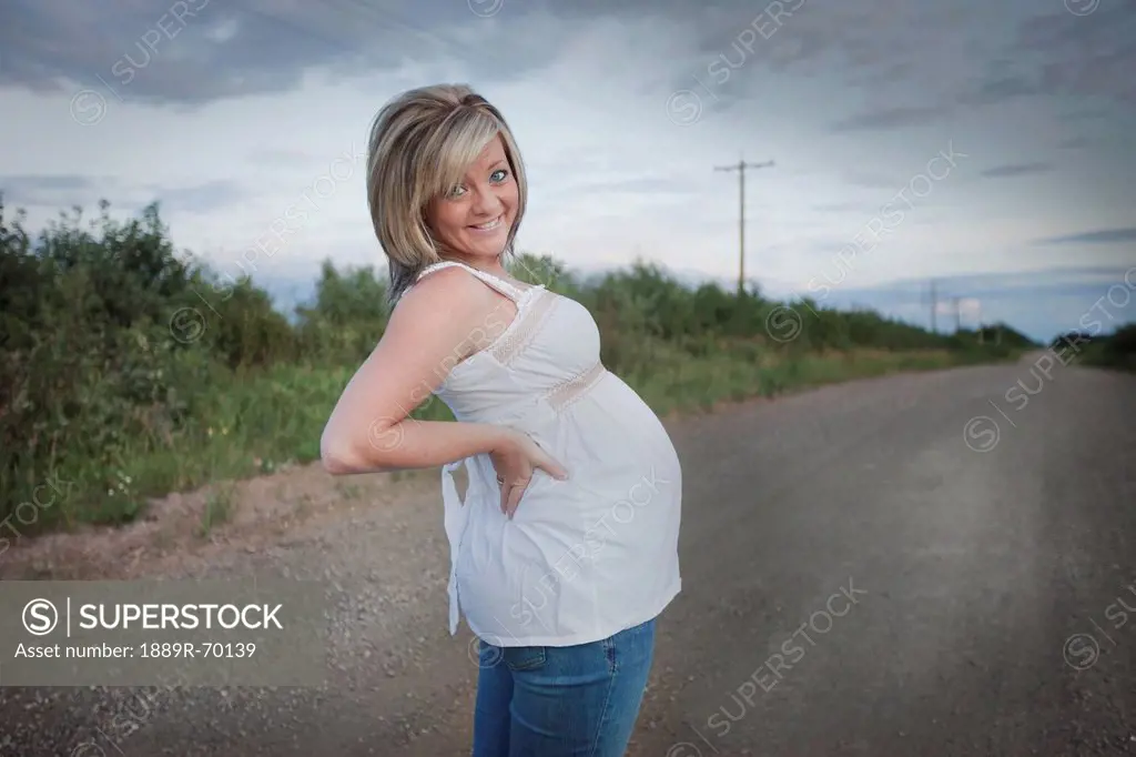 a pregnant woman stands on a dirt road, edmonton alberta canada
