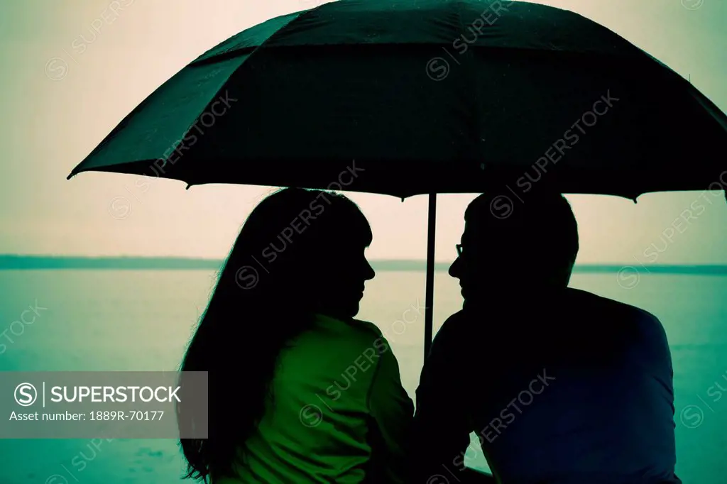 a couple sits under an umbrella at the water´s edge, bellingham washington united states of america