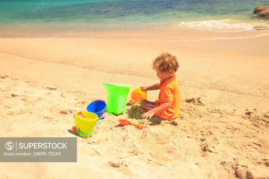 a young boy plays in the sand with his sand toys at cabo pulmo, baja california sur mexico