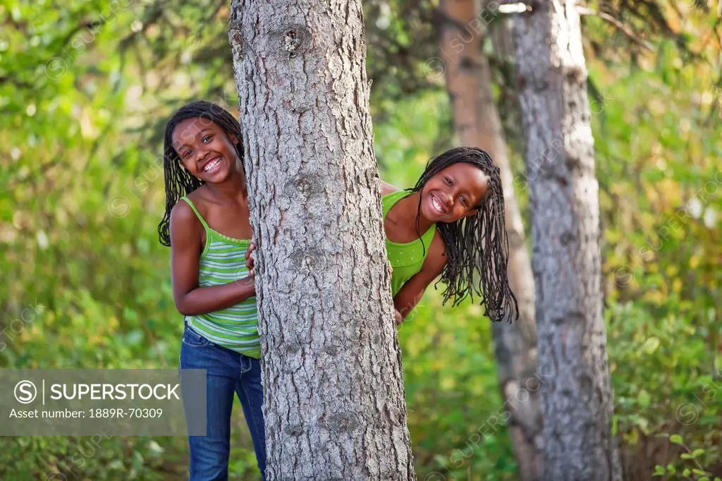 sisters hiding behind a tree in a park, edmonton alberta canada