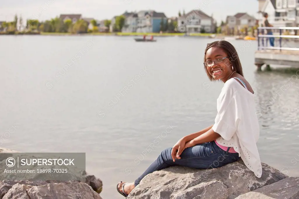 a teenage girl relaxing on the rocks on shore of a residential lake, edmonton alberta canada