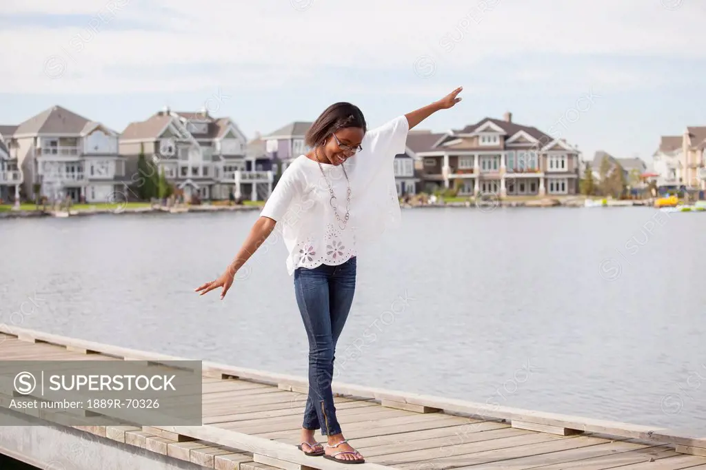 teenage girl balancing on the rail of a pier in a residential lake neighborhood, edmonton alberta canada