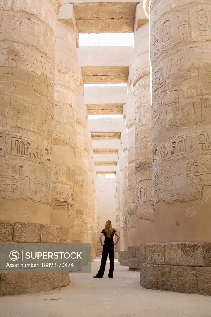 a woman tourist stands at the base of the massive columns in the temples of karnak on the east bank of luxor along the nile river, egypt