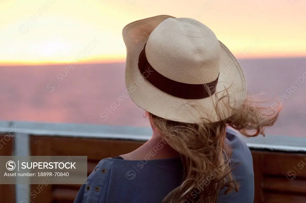 a young woman wearing a hat and watching the sunset, galapagos equador