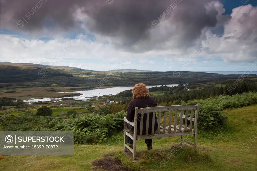 a woman sits on a wooden bench overlooking a landscape, isle of mull scotland