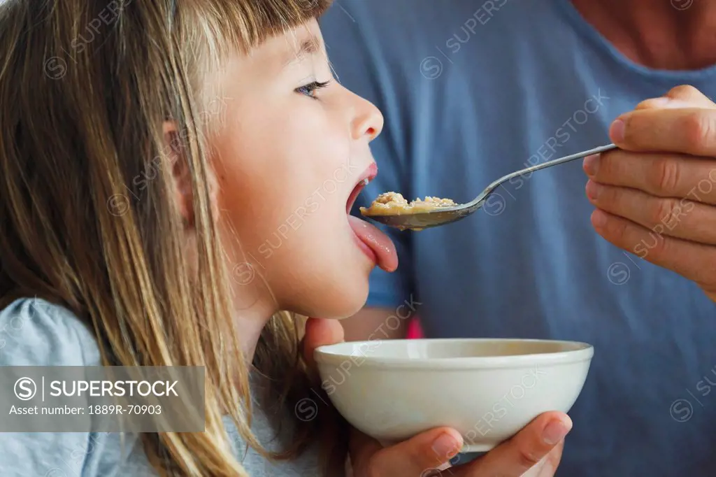 child being spoon fed food from a bowl by her father, spain