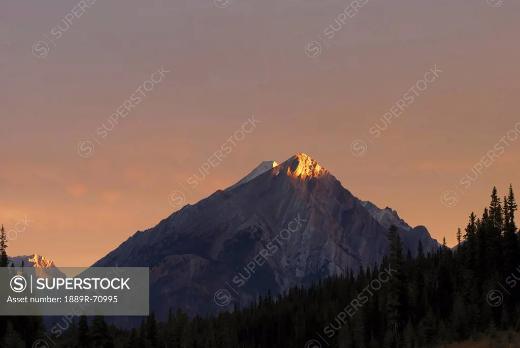 sunrise lights up a mountain peak, alberta canada