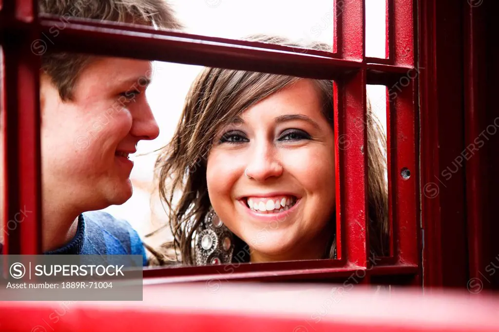a young couple smiling through a red english phone booth, bellingham washington united states of america