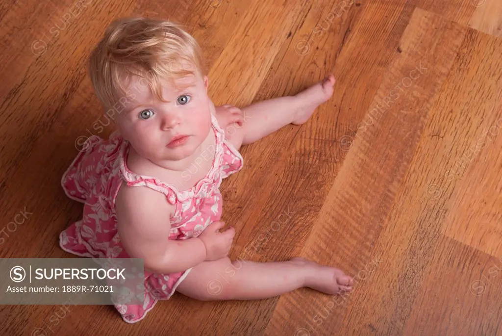 a baby girl sits on a hardwood floor, alberta canada