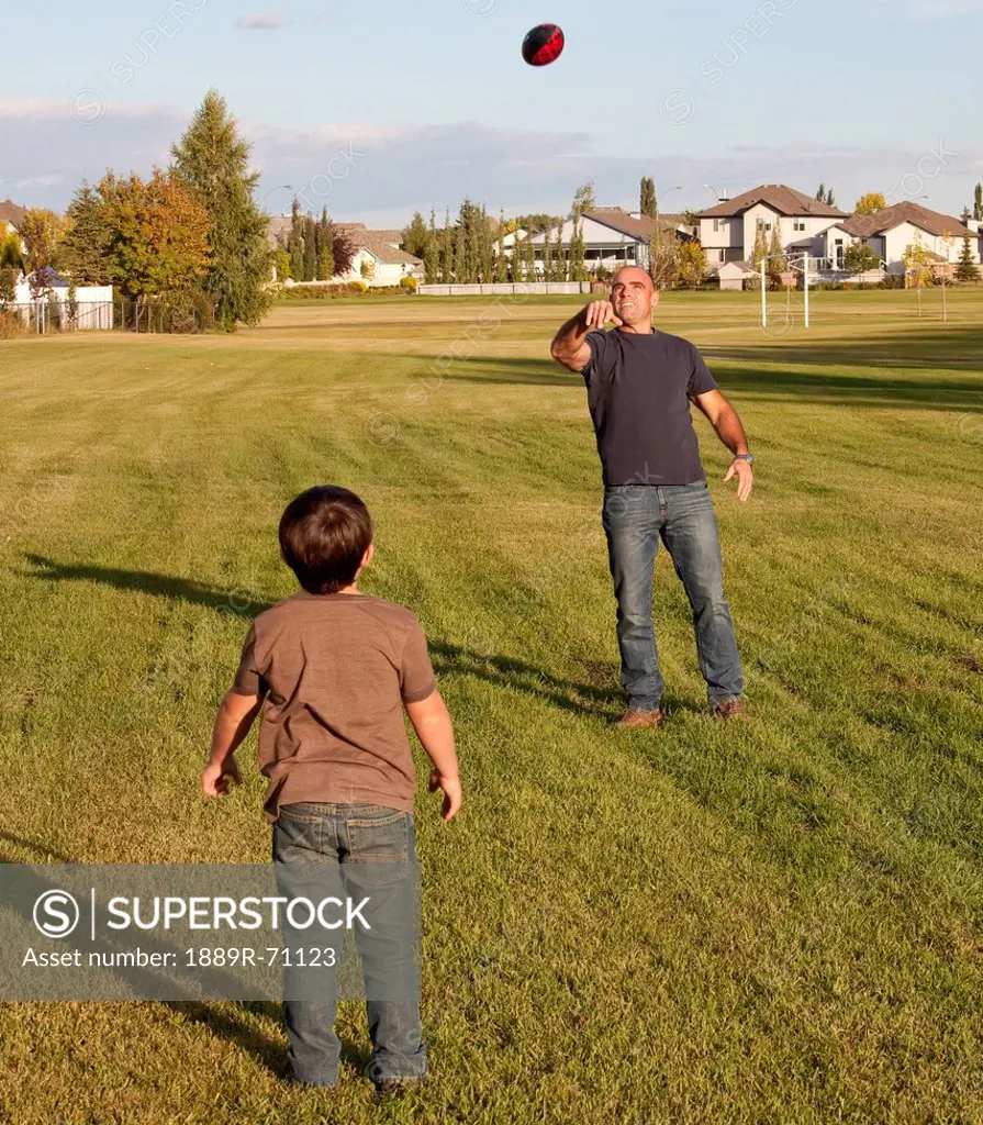 father and son playing football in a park, beaumont alberta canada