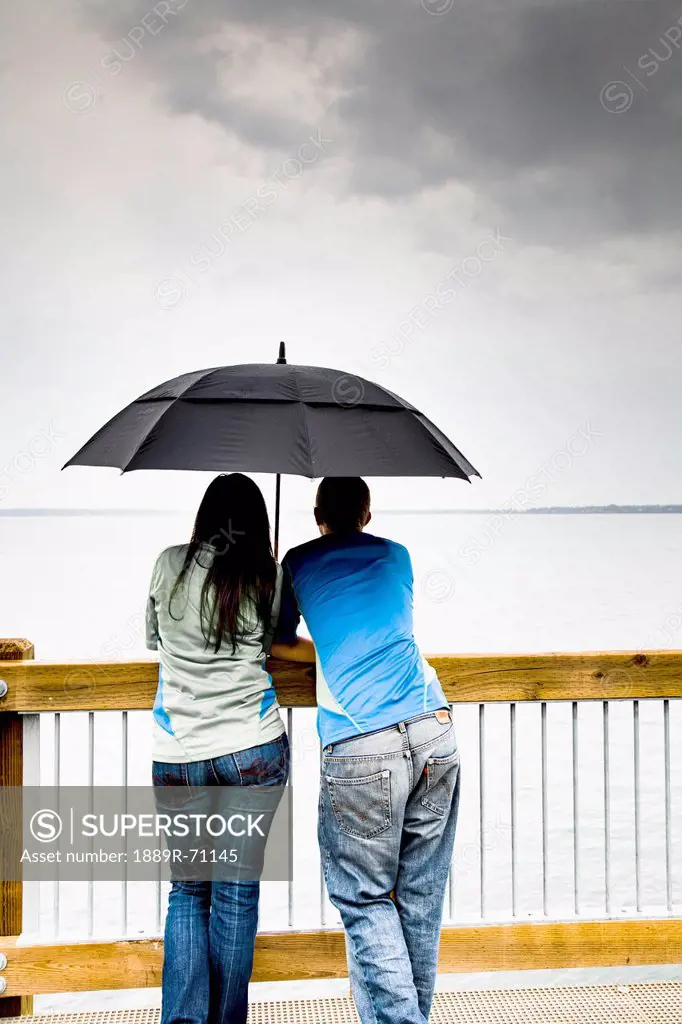 a young couple stands under an umbrella at the shoreline, bellingham washington united states of america