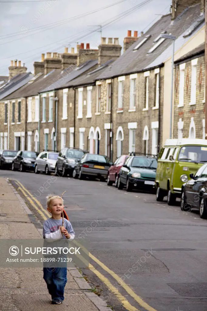 a young boy walks down the street with a stick, cambridge united kingdom