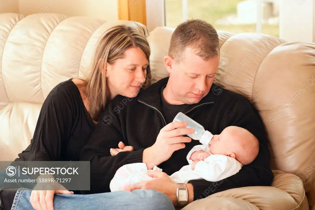 a father feeding his newborn baby from a bottle as the mother looks on, dundas minnesota united states of america