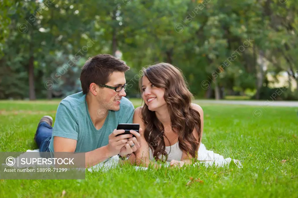 young couple looking at text messages together in the park, edmonton alberta canada