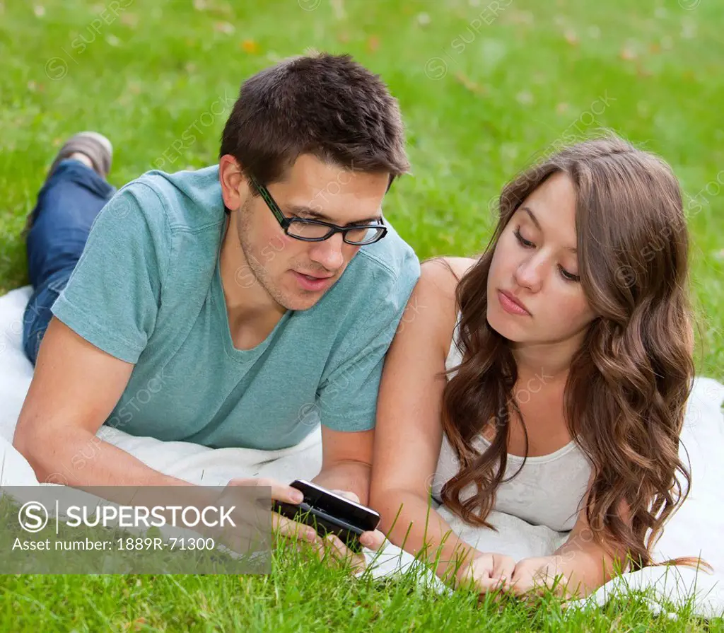 young couple looking at text messages together in the park, edmonton alberta canada