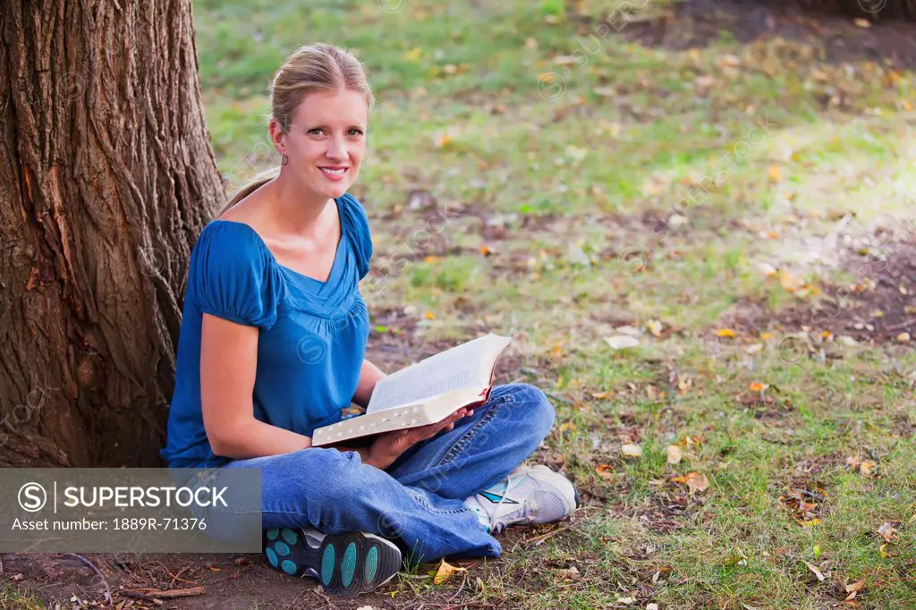 woman reading her bible in the park beside a tree, edmonton alberta canada