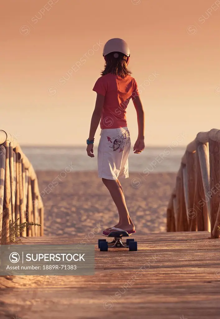 a young person skateboarding with bare feet over a wooden boardwalk towards the beach, tarifa cadiz andalusia spain
