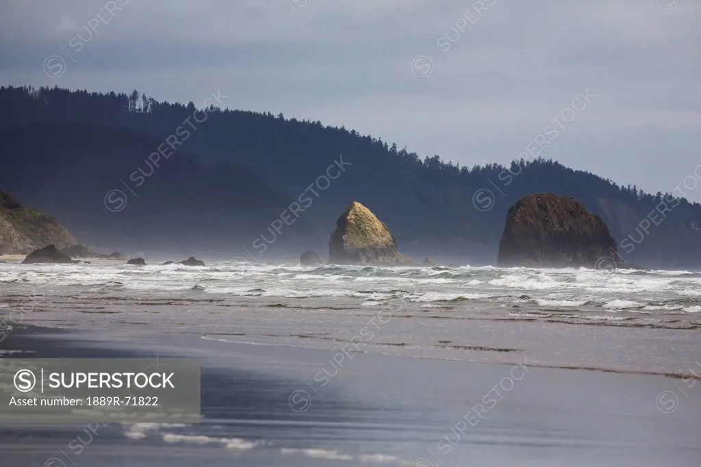 rock formations in the ocean with waves on the beach, cannon beach oregon united states of america