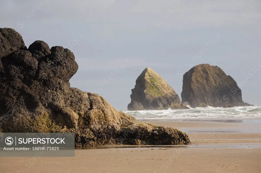 rock formations in the ocean with waves on the beach, cannon beach oregon united states of america