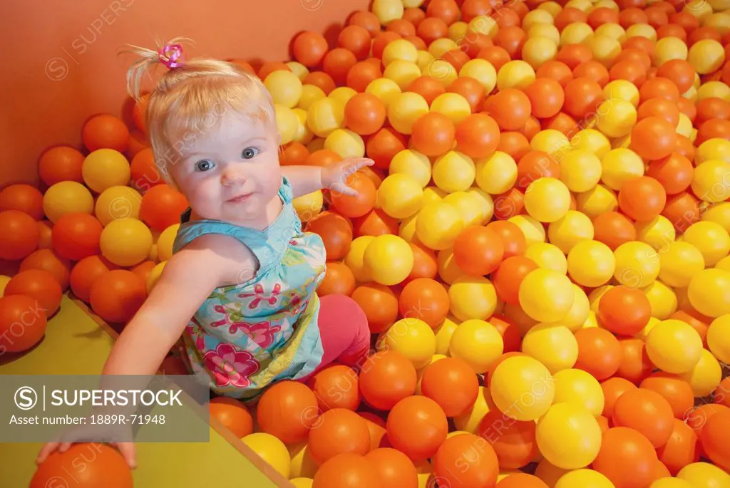 a baby girl plays in a pit full of orange and yellow balls, alberta canada