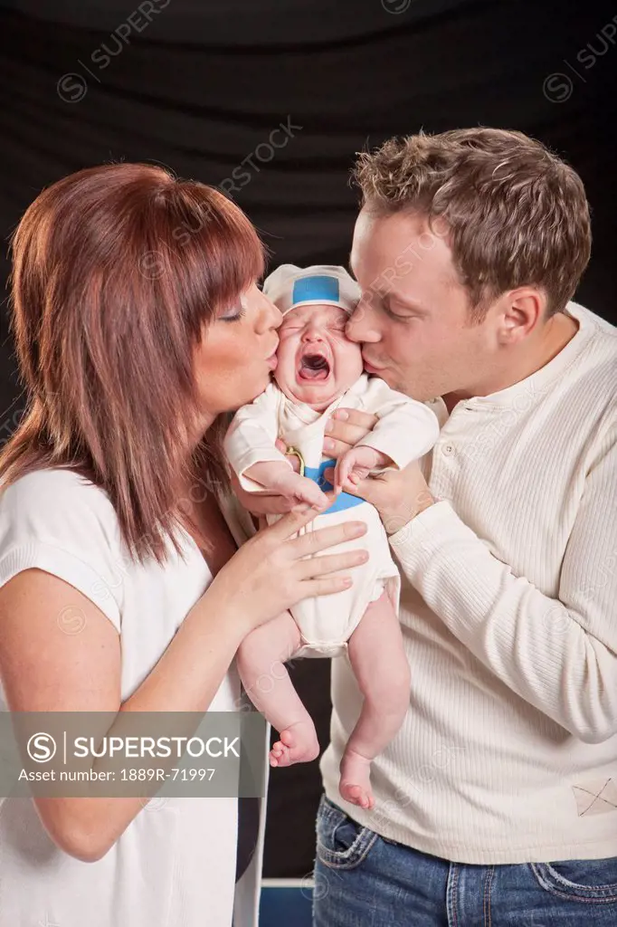 a mother and father kiss a crying newborn baby, edmonton alberta canada