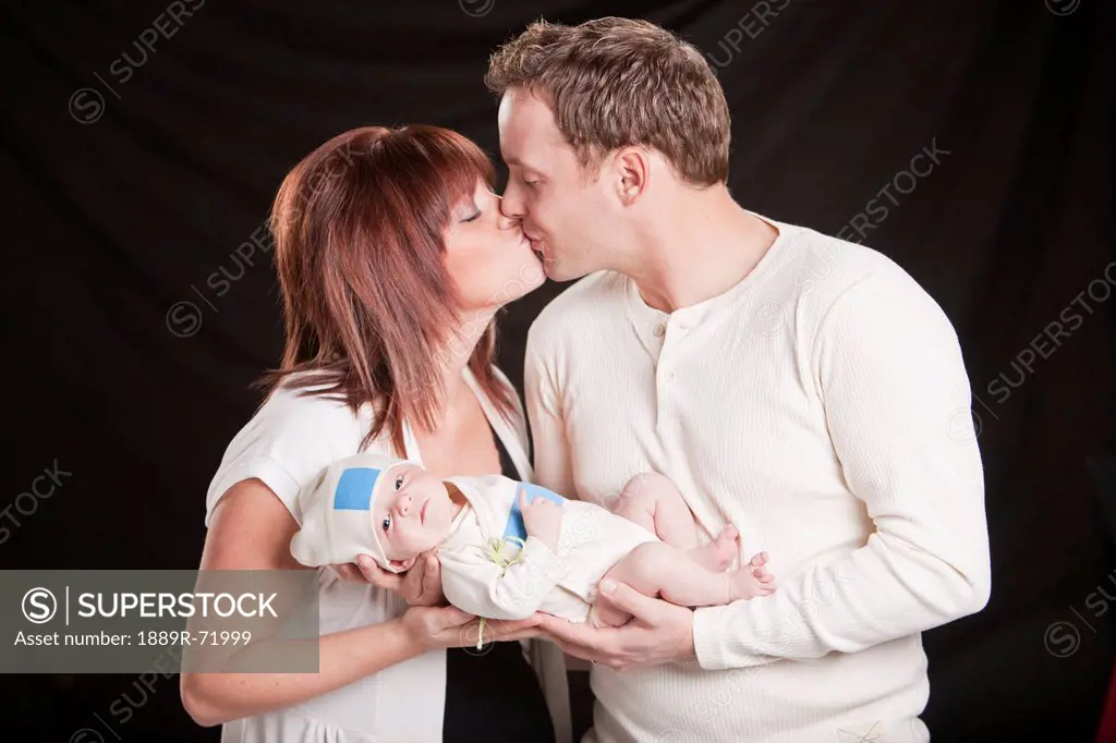 a mother and father kiss while holding a newborn baby, edmonton alberta canada