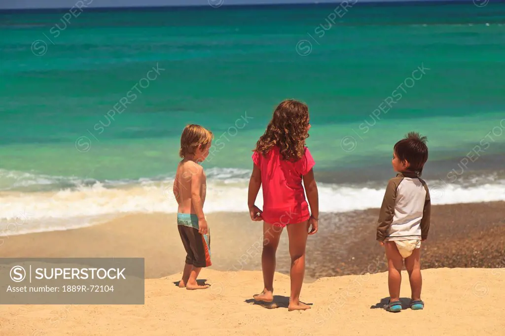 children standing on a beach at the water´s edge at cabo pulmo, baja california sur mexico