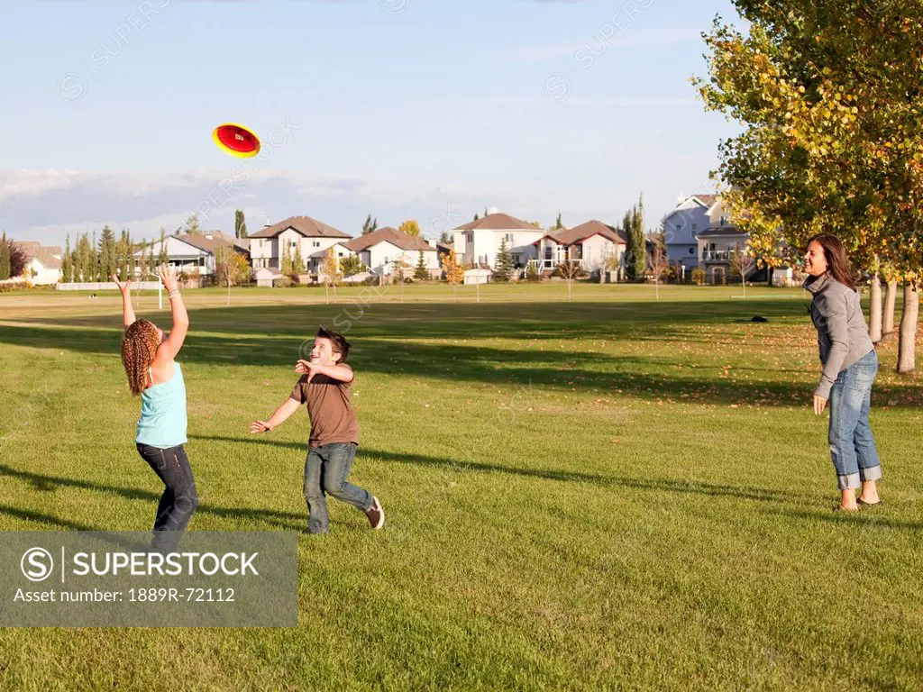 mother throwing flying disc to children in a park, beaumont alberta canada