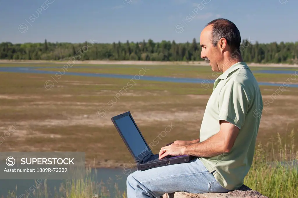 man typing on a laptop overlooking a river delta, calgary alberta canada