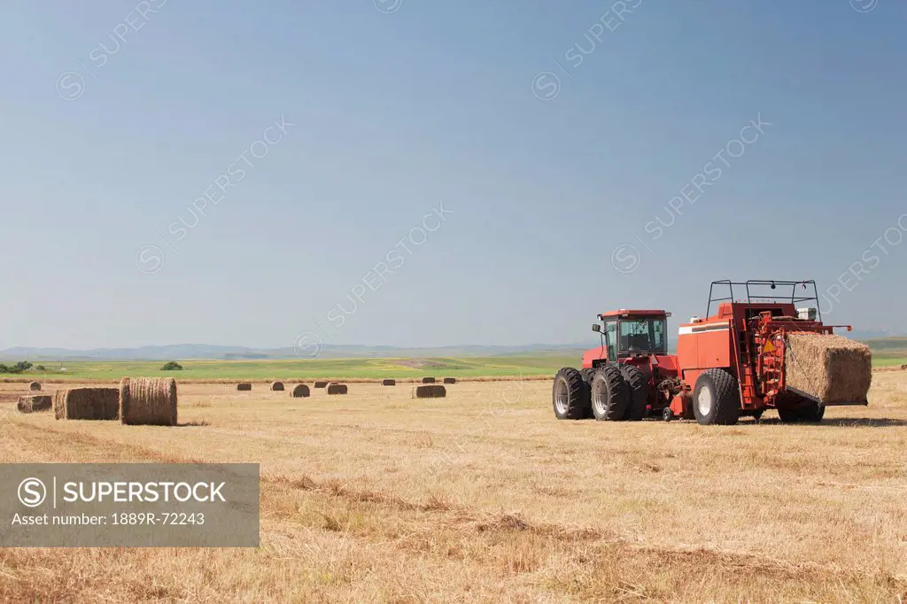 hay baler in a field with blue sky, alberta canada