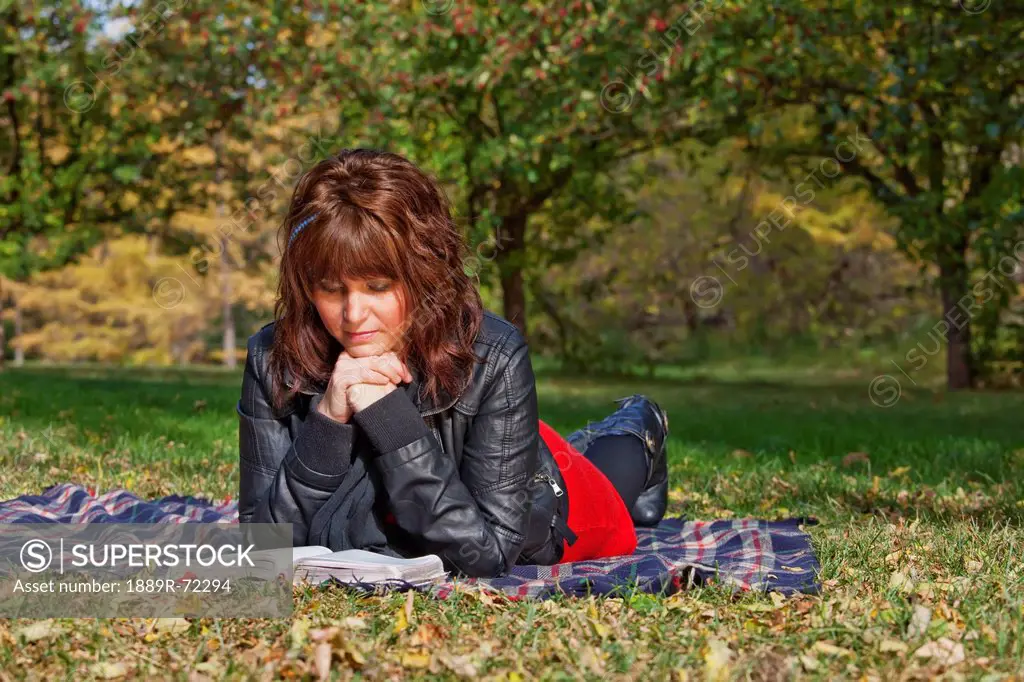 a young woman reading a bible and meditating in a park, edmonton alberta canada