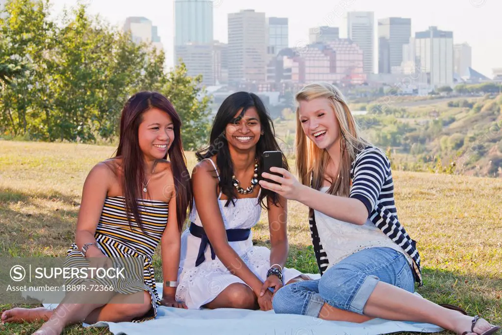 friends looking at smart phones in a city park with the skyline in the background, edmonton alberta canada